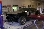 Black sports car on a tow truck inside a garage, with the front bumper damaged