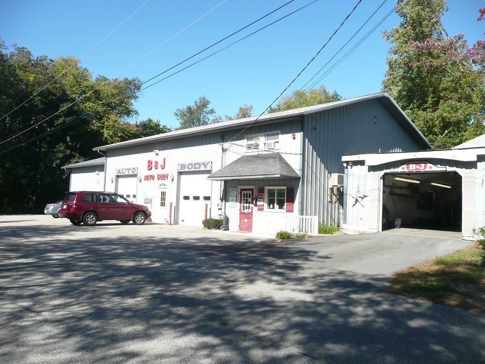 Small gray auto repair shop with a red car parked outside on a sunny day.