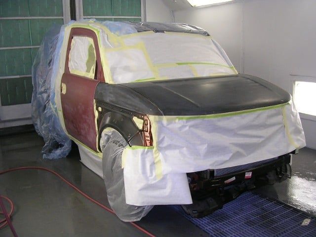 Car covered in masking paper and tape inside a spray booth, being painted black and maroon