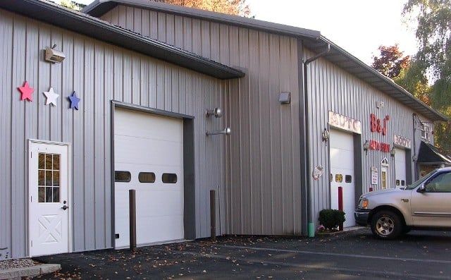 Gray metal industrial building with white garage doors, star decorations, and a pickup truck parked outside