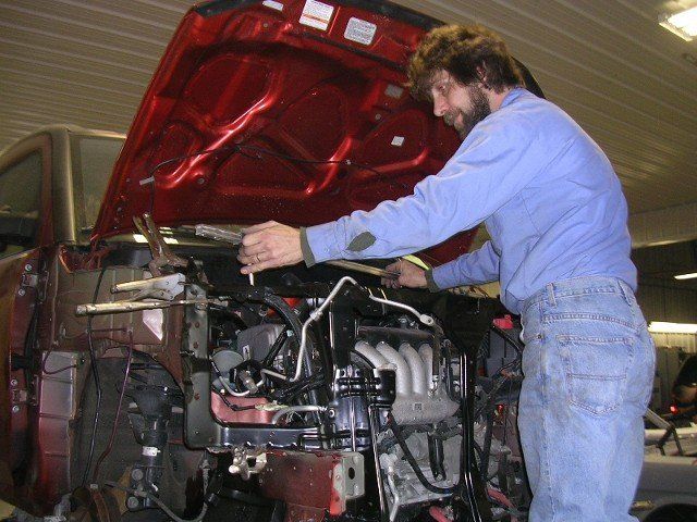 Mechanic working on a car engine with the hood raised in a garage.