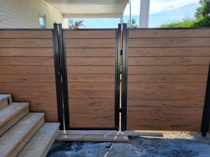 Portail en bois avec cadre en métal noir dans une allée extérieure clôturée, à côté d'escaliers et d'un mur de maison