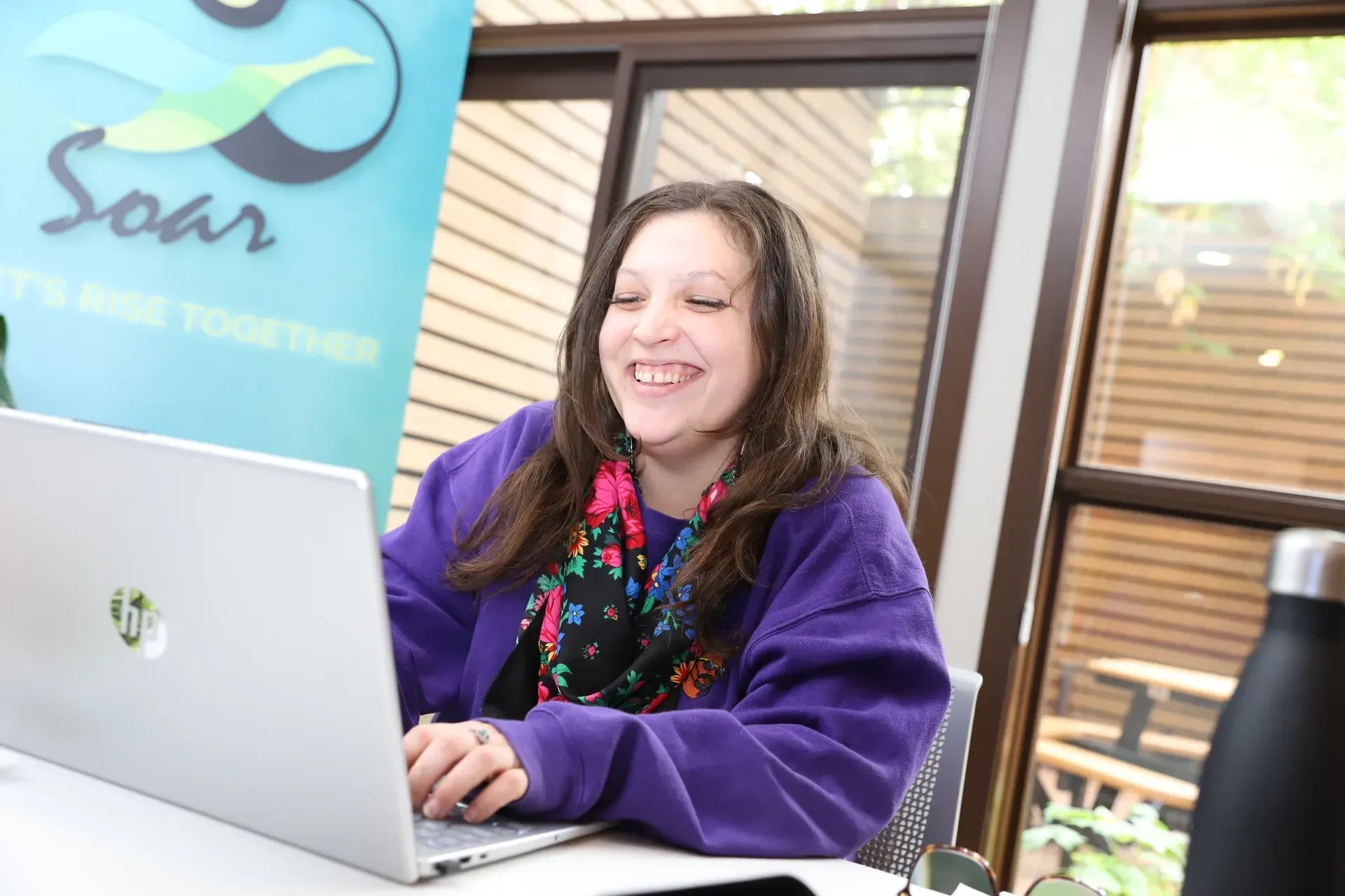 Woman in purple sweatshirt smiles while using a laptop. 