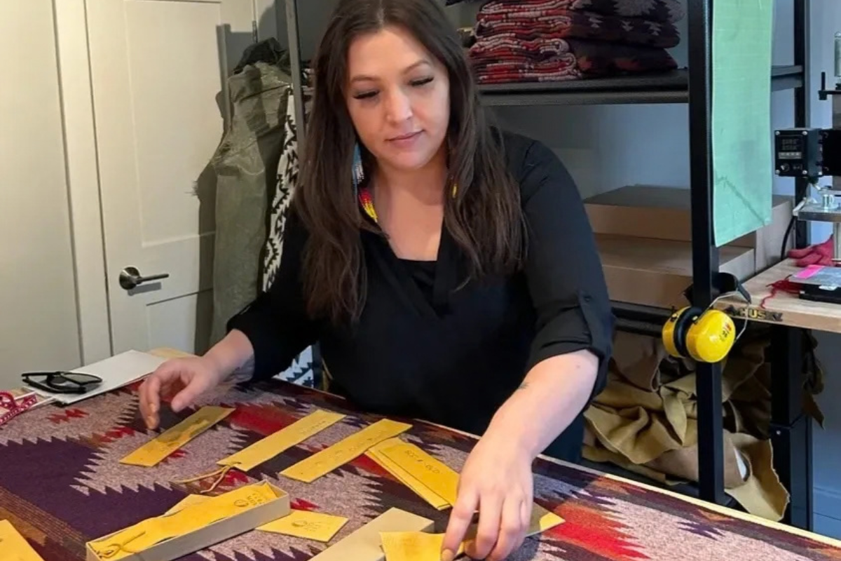 Woman arranging yellow leather pieces on a colorful fabric, near shelves and tools.