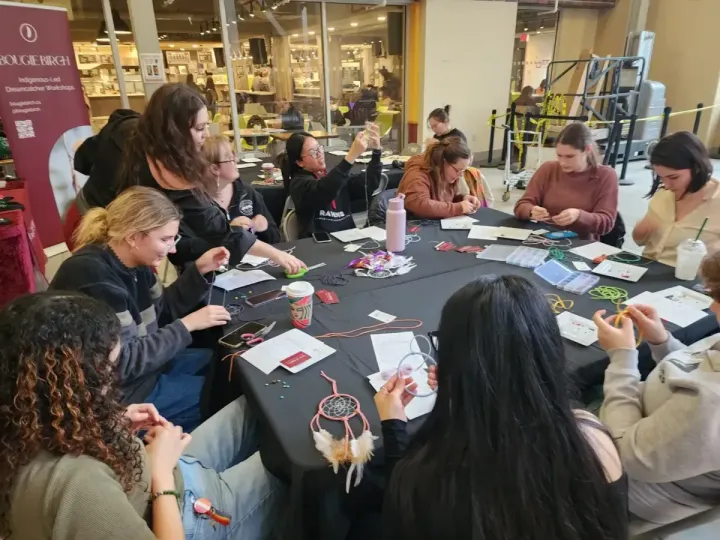 People seated at a table crafting jewelry in a workshop setting.