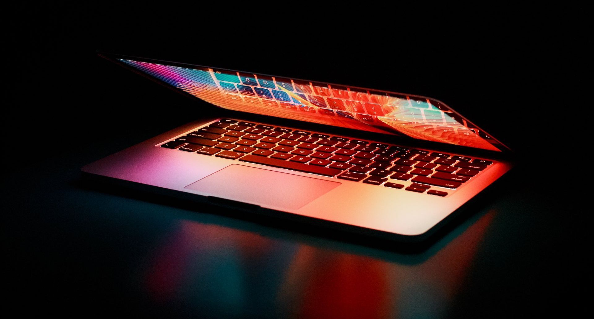 Laptop with glowing keyboard and screen, set against a dark background, radiating vibrant colors.