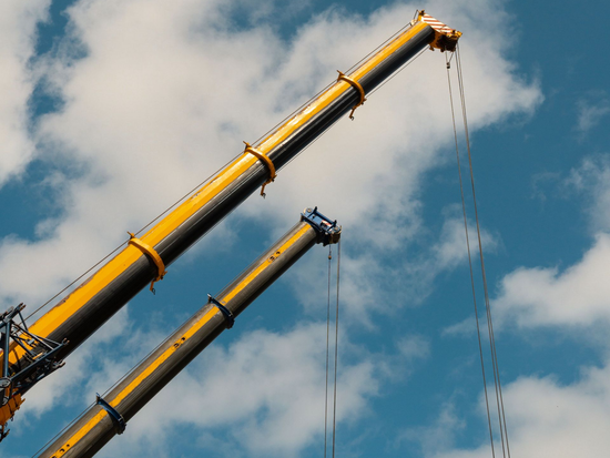 Two cranes next to each other with the sky in the background.