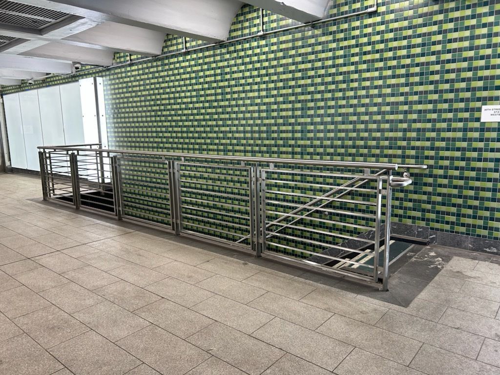 A staircase with a stainless steel railing and a green tiled wall.