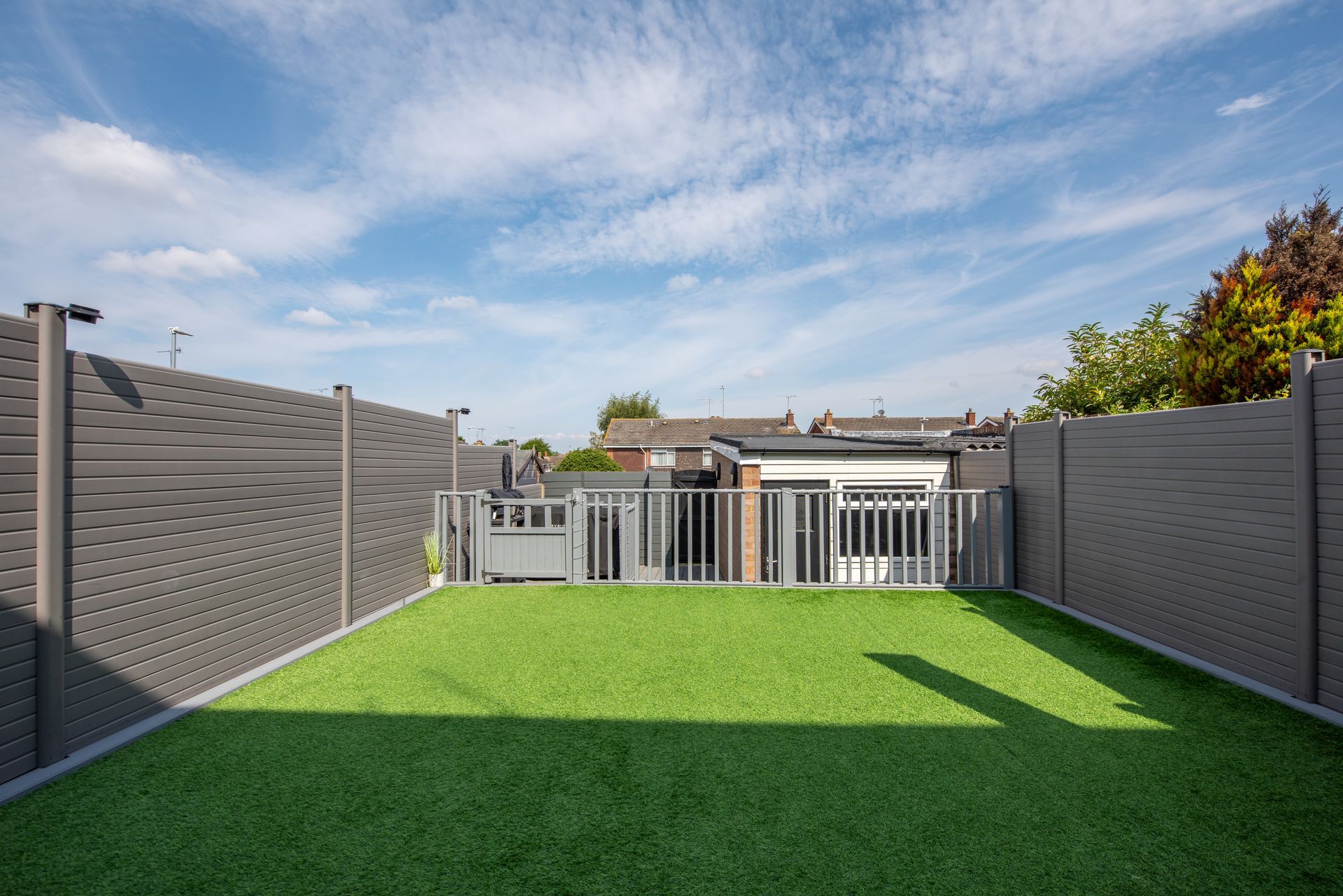 Small backyard with grey composite fencing and artificial grass landscaping.