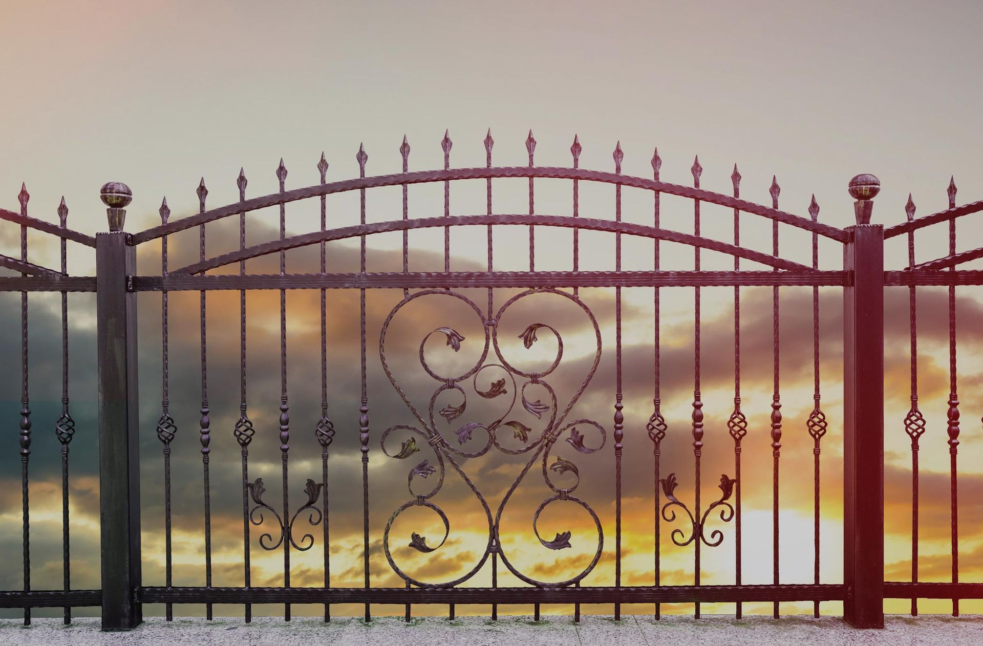 A wrought iron fence with a sunset in the background