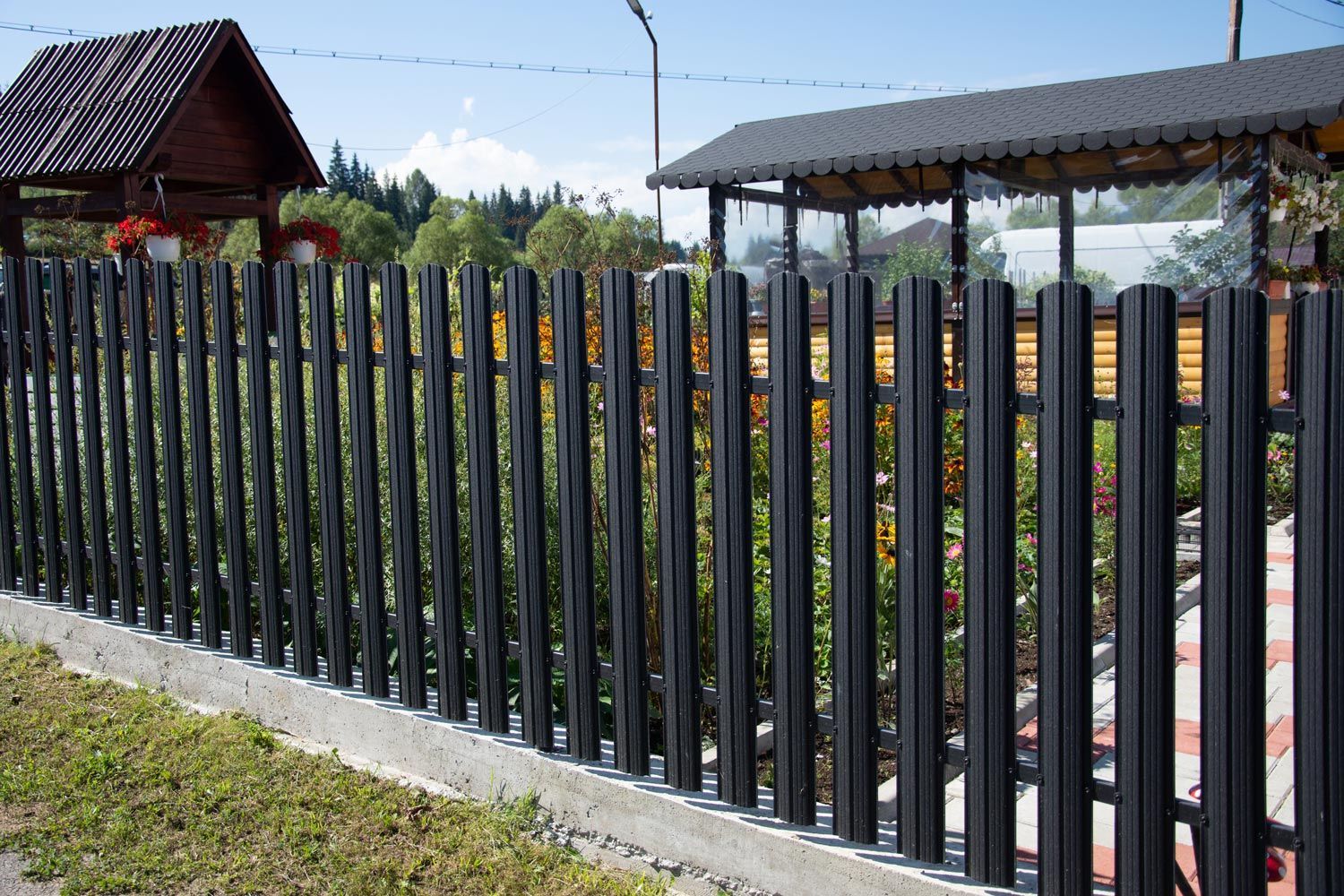 A black metal fence is surrounding a yard with a house in the background.