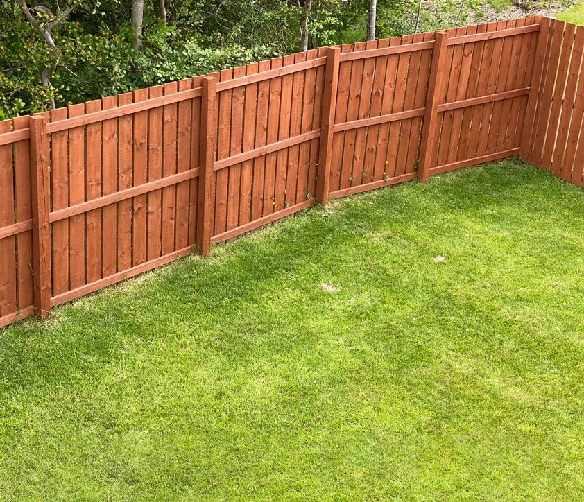 A wooden fence surrounds a lush green lawn in a backyard. A wooden fence surrounds a lush green lawn in a backyard.