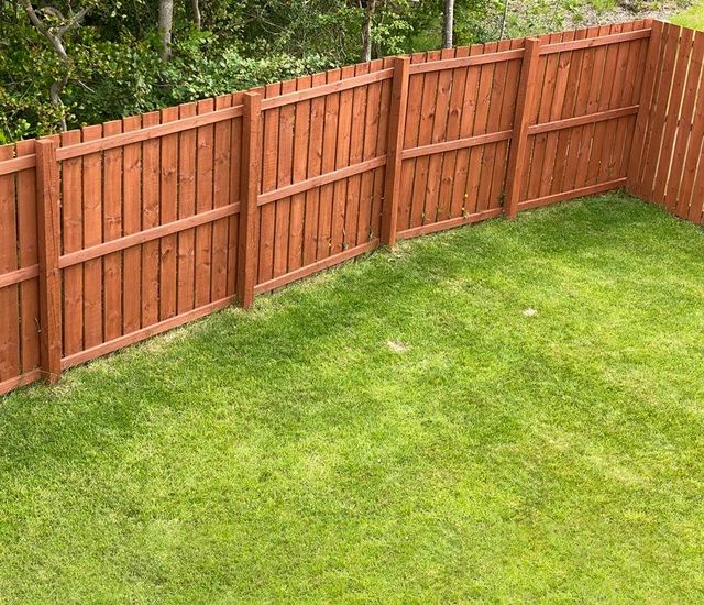 A wooden fence surrounds a lush green lawn in a backyard. A wooden fence surrounds a lush green lawn in a backyard.