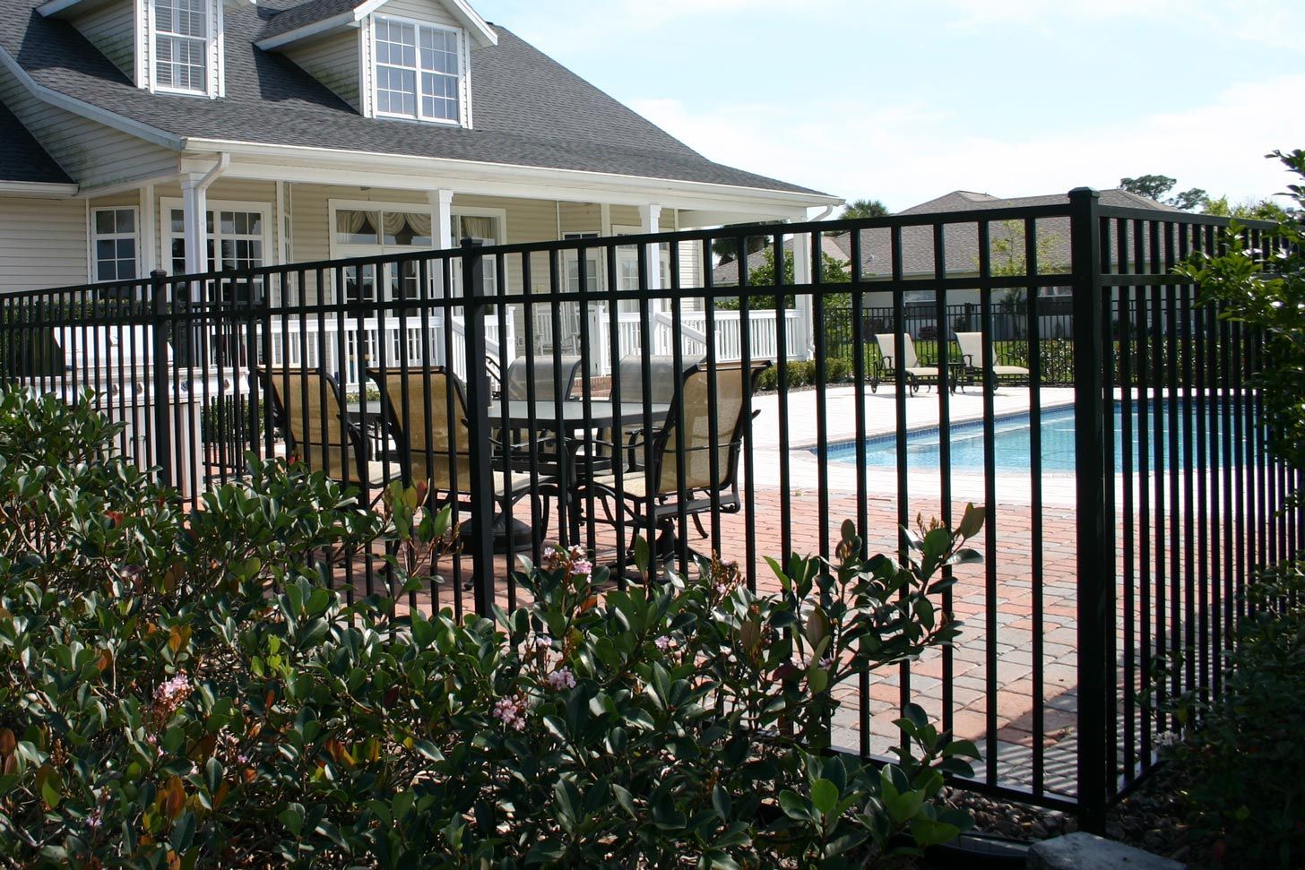 A black fence surrounds a swimming pool in front of a house