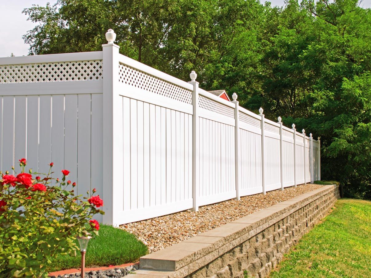 A white fence surrounds a stone wall in a yard