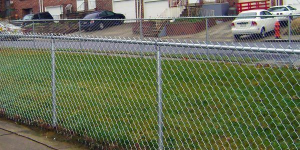 A chain link fence surrounds a lush green field with cars parked behind it.