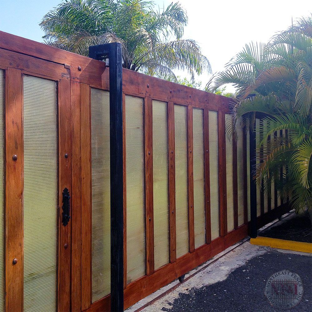 A wooden fence surrounds a driveway with palm trees in the background