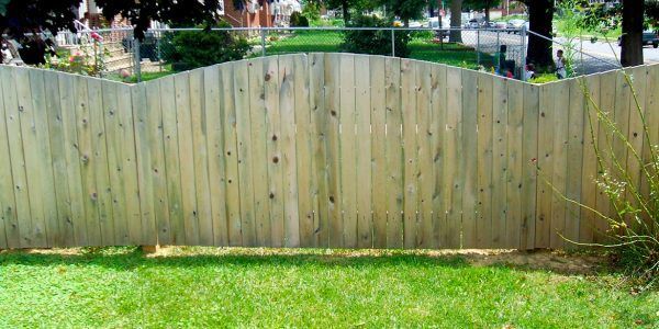 A wooden fence is in the middle of a lush green yard.