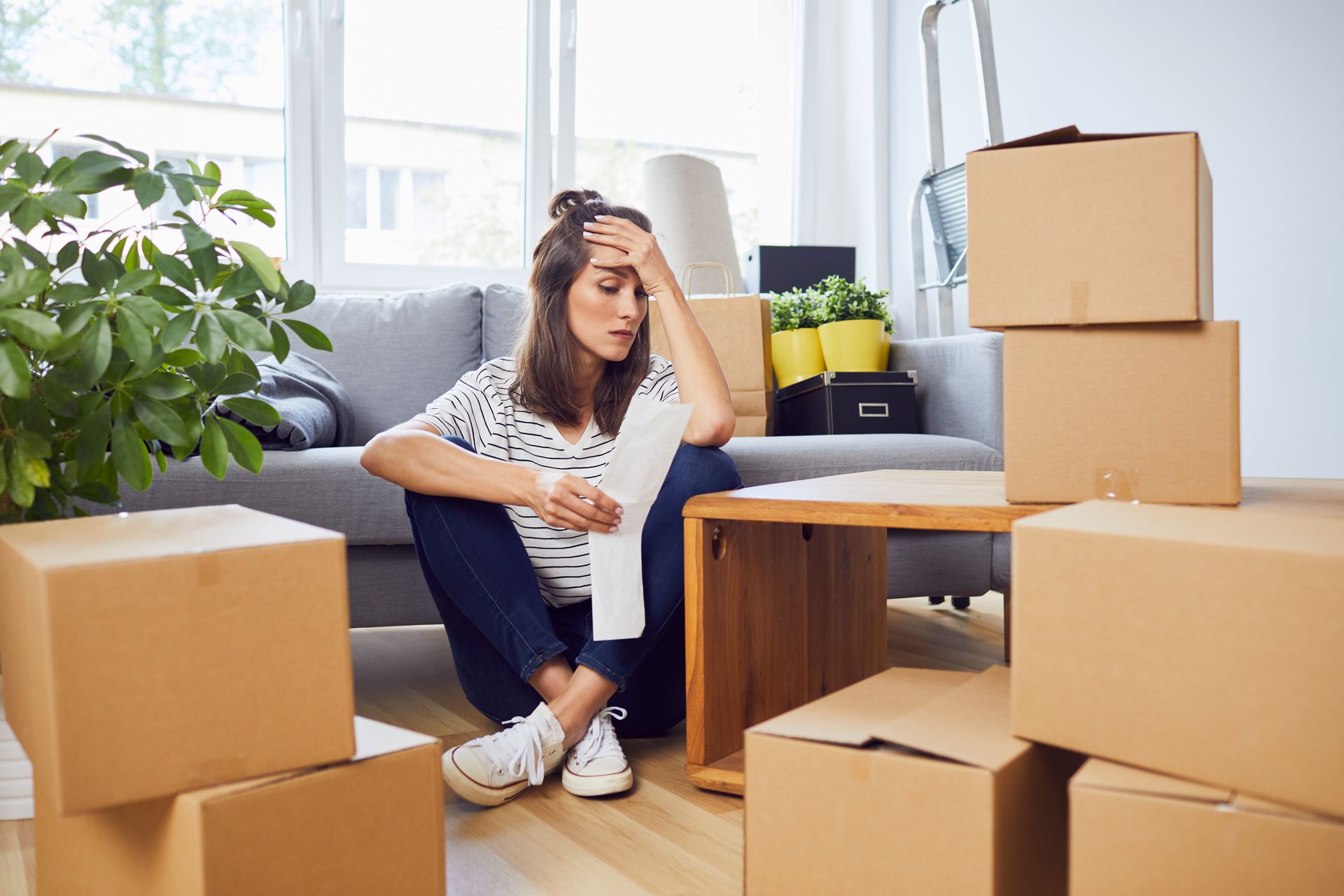 Une femme est assise par terre dans un salon entourée de cartons.