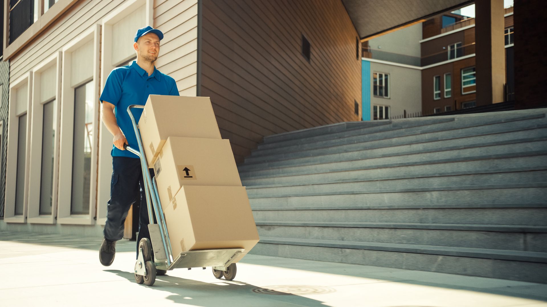 Un livreur pousse un chariot avec des cartons dessus.