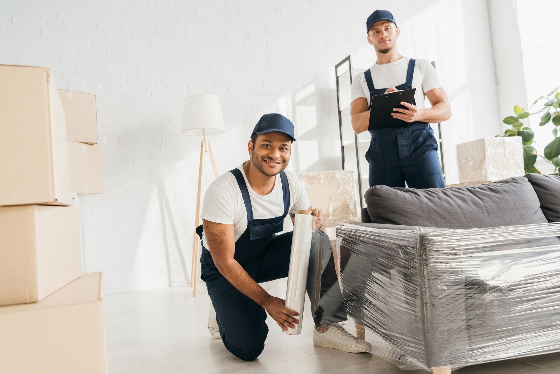 Deux hommes enveloppent un canapé dans du film plastique dans un salon.