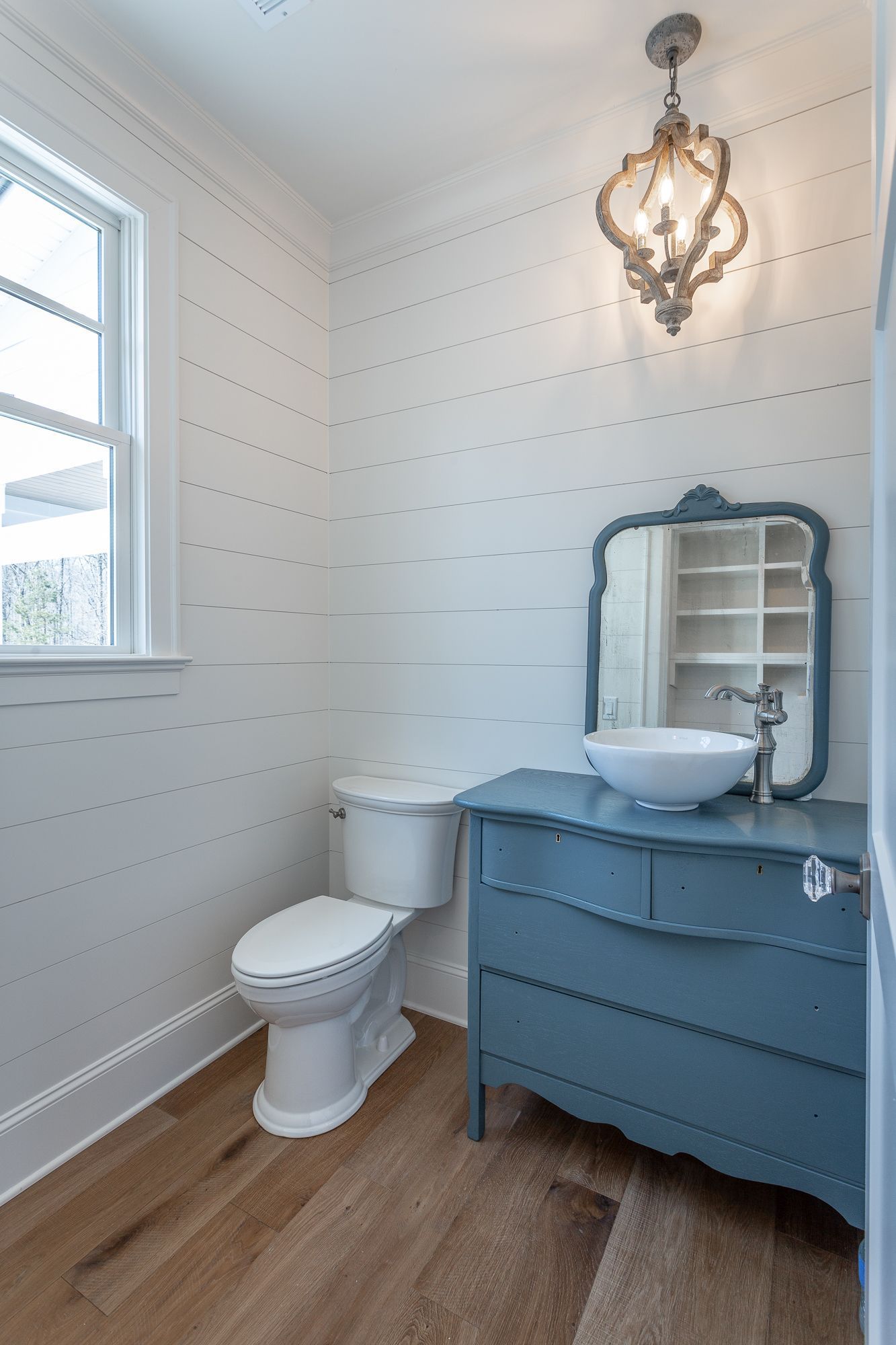 A bathroom with a toilet , sink , mirror and dresser.