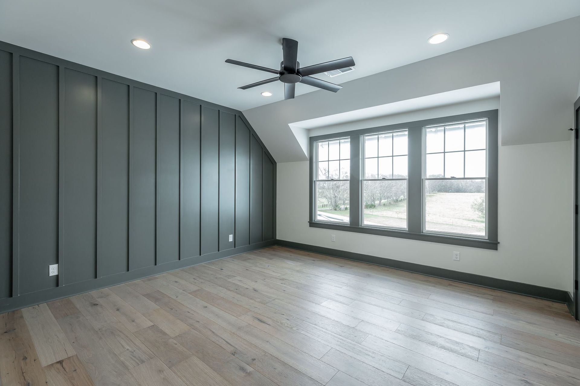 An empty room with a ceiling fan and three windows.