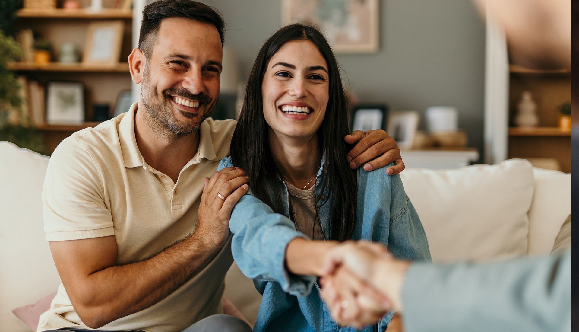 Happy couple shaking hands with an unseen person, smiling indoors.