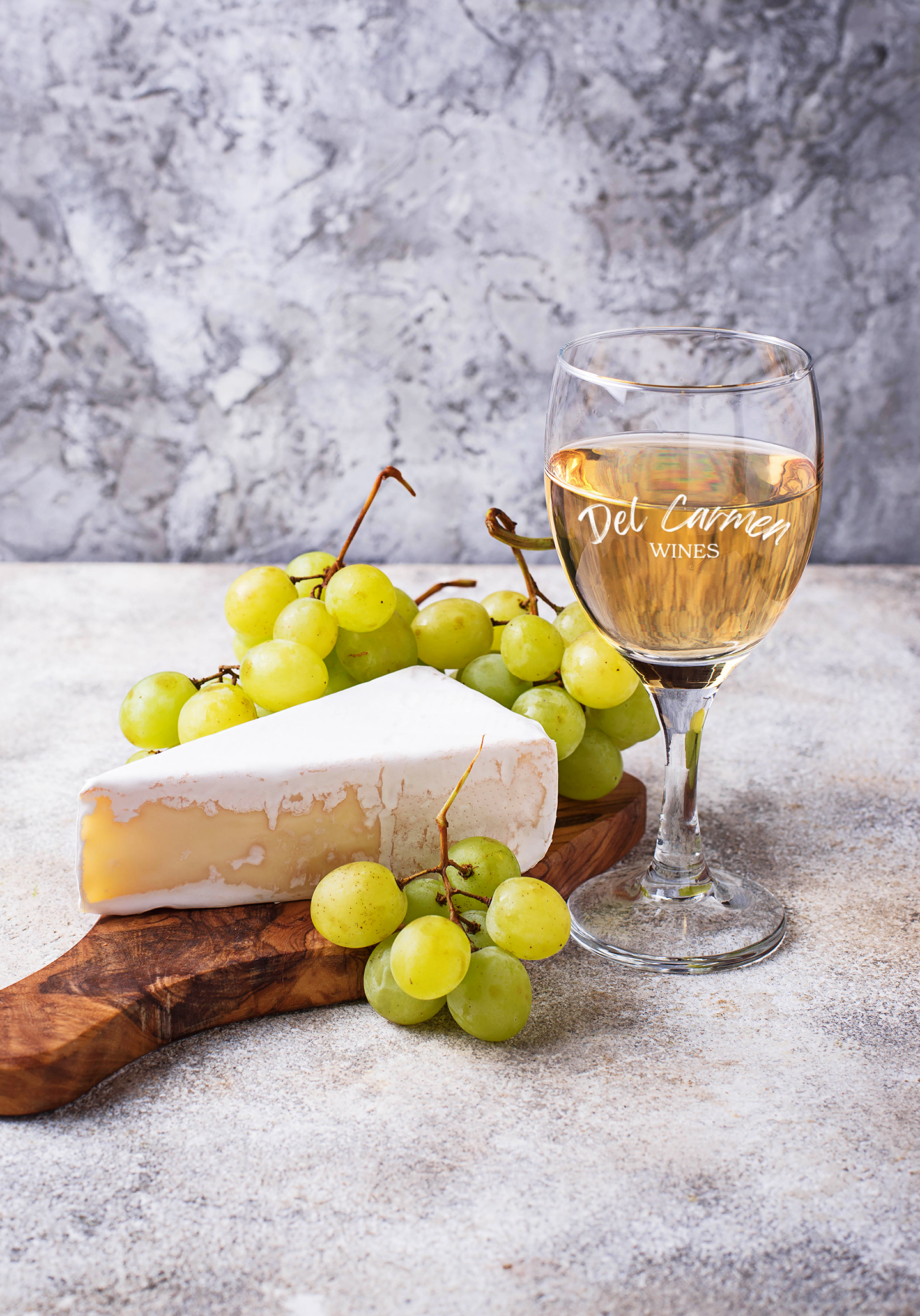 A bottle of white wine with a blue label, a glass of wine, and clusters of red and green grapes on a burlap surface.