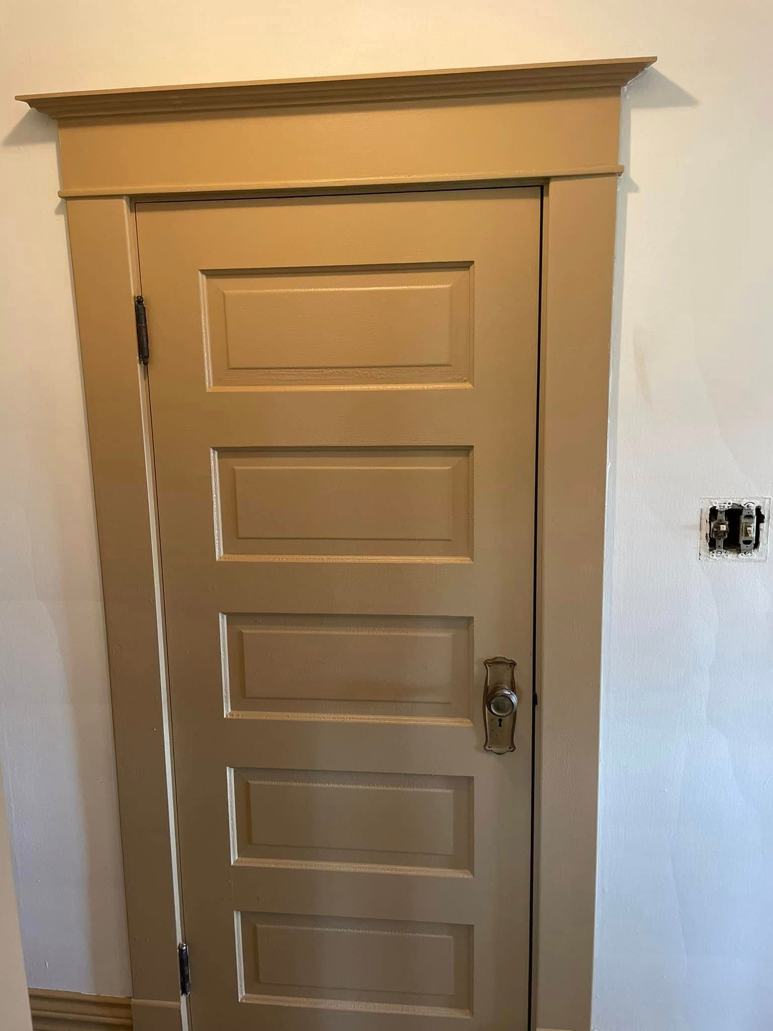 Small beige door with decorative trim in a white wall, partially open with a visible handle.