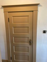 Small beige door with decorative trim in a white wall, partially open with a visible handle.