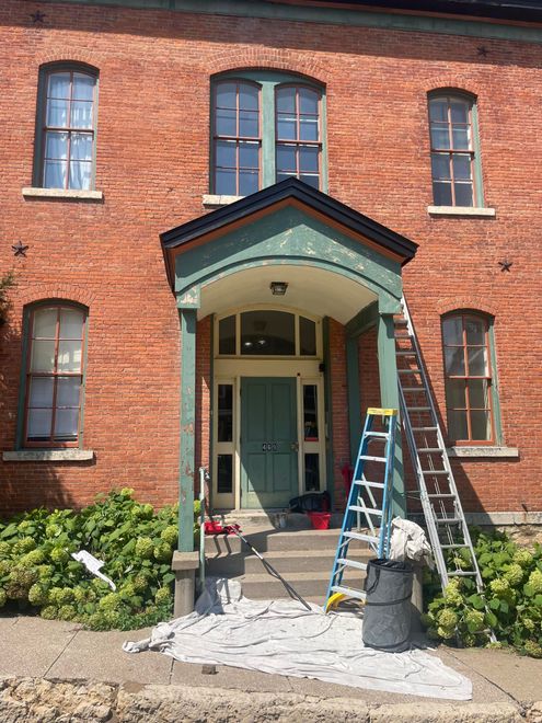 Brick building entrance under repair, with scaffold, ladder, and construction debris on the steps