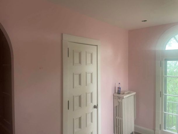 Pink bedroom with white door, radiator, and arched window overlooking greenery