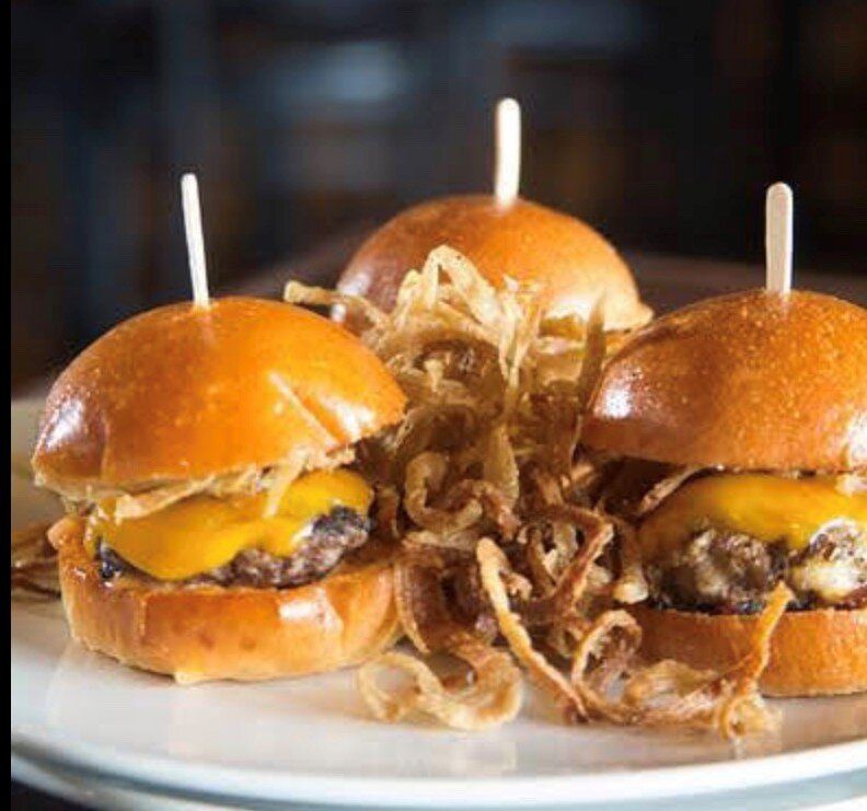 Three mini cheeseburgers on a plate, topped with crispy onion strings and toothpicks