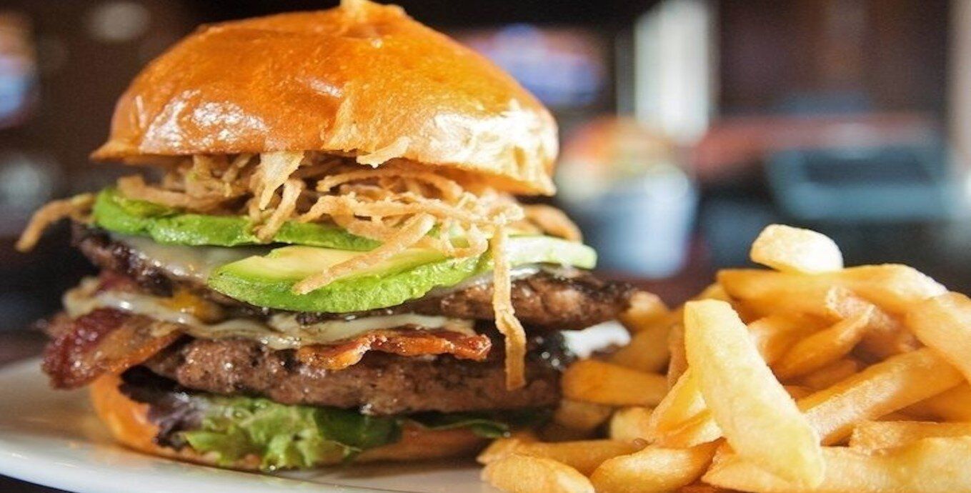 Close-up of a burger with fries on a plate, topped with lettuce and other fixings.