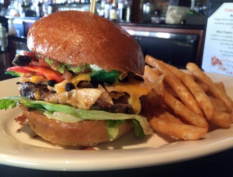 Cheeseburger on a plate with lettuce, tomato, bacon, and fries on the side