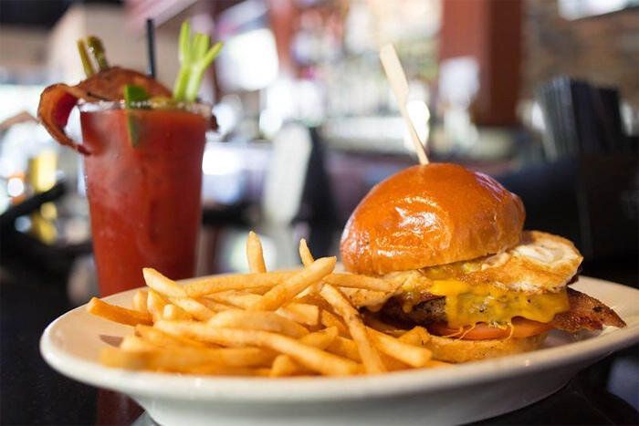 Burger and fries on a plate with a red cocktail in a restaurant setting
