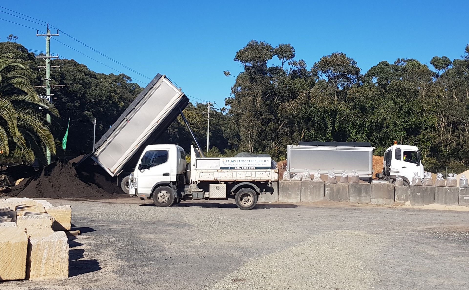 Truck dumping soil onto a pile; another truck and concrete blocks nearby - Palms Landscape Supplies in Forster, NSW