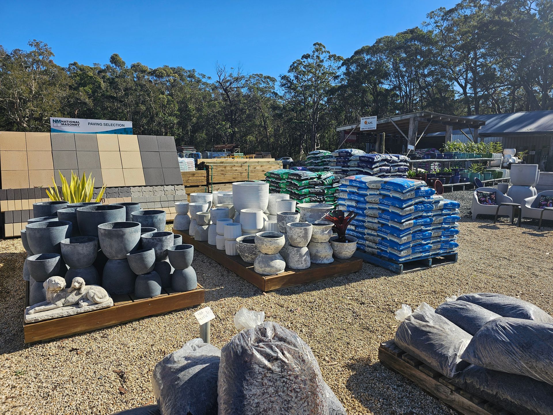 Outdoor garden centre displaying pots, pavers, soil bags under a clear sky - Palms Landscape Supplies in Forster, NSW