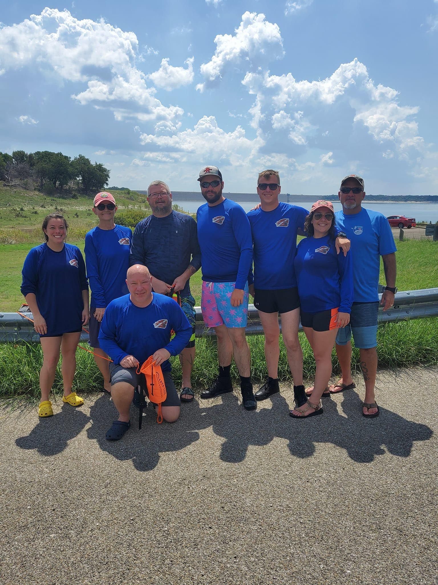 Group of people in blue shirts posing outdoors, sunny day.