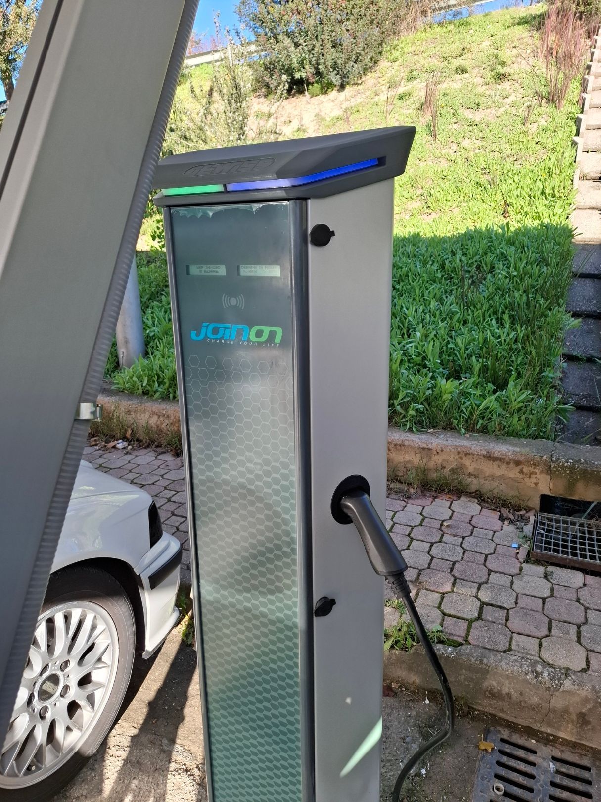 Stazione di ricarica per veicoli elettrici con luci verdi e blu, con un'auto collegata.