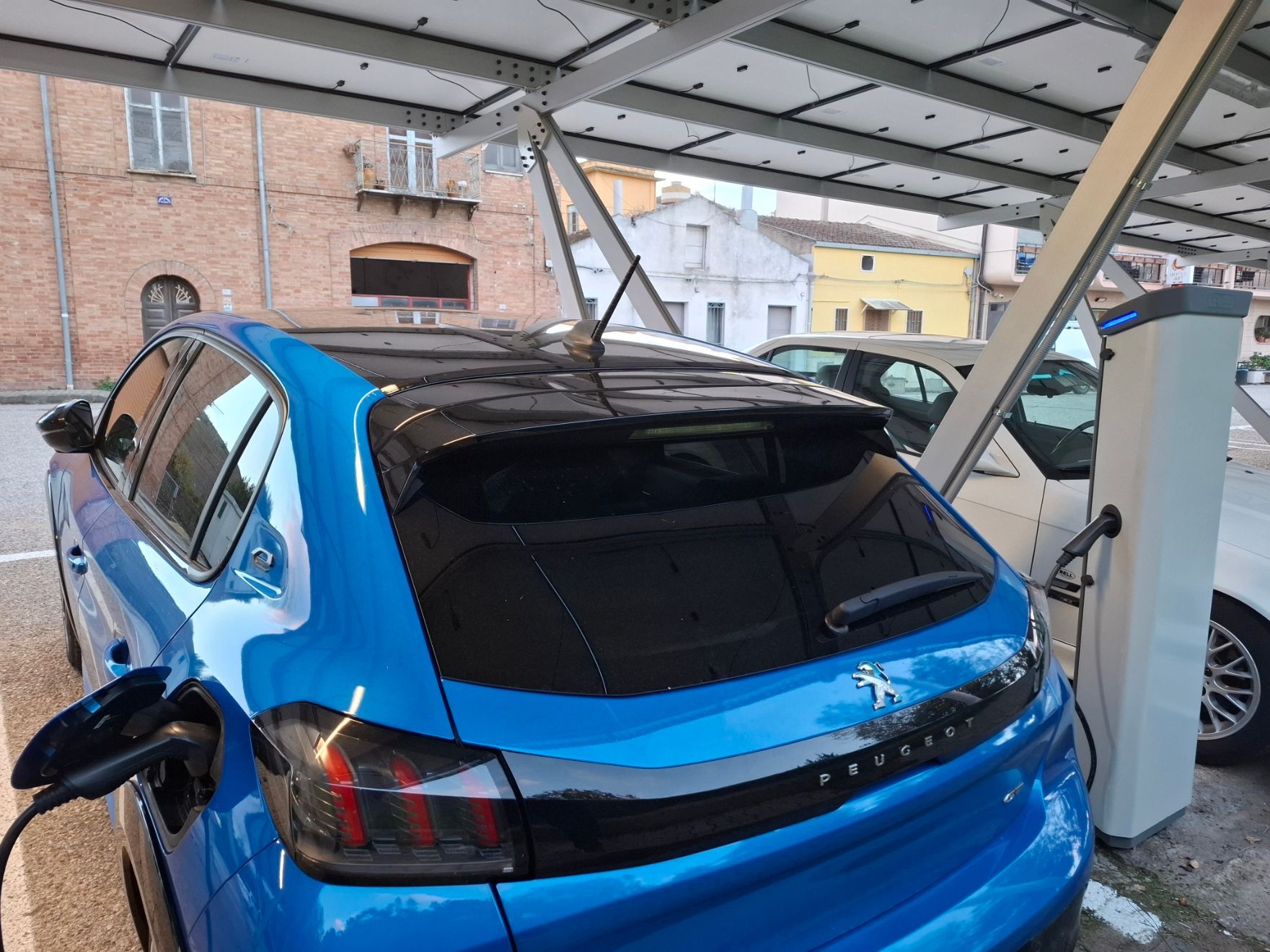 Un'auto elettrica blu in ricarica sotto i pannelli solari in un parcheggio.