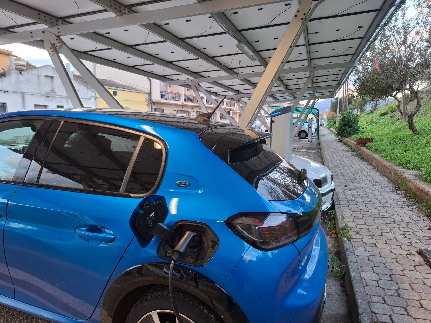 Auto elettrica blu in ricarica sotto i pannelli solari, all'aperto.