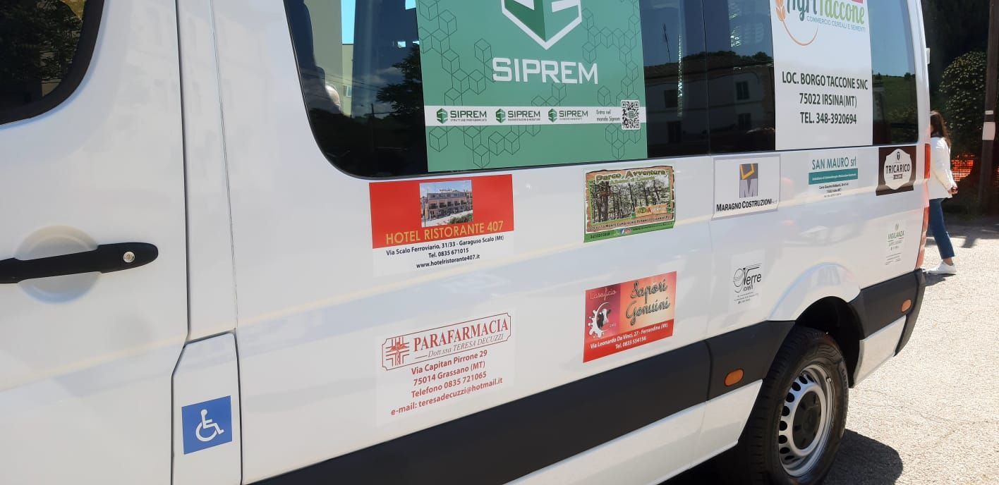 Furgone bianco con vari adesivi, tra cui uno per l'accessibilità. Una persona cammina sullo sfondo.