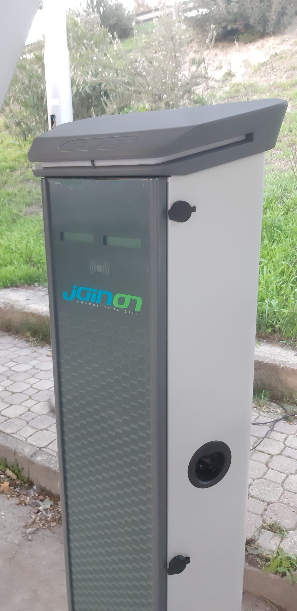 Stazione di ricarica per veicoli elettrici con facciata grigia e verde, all'aperto.