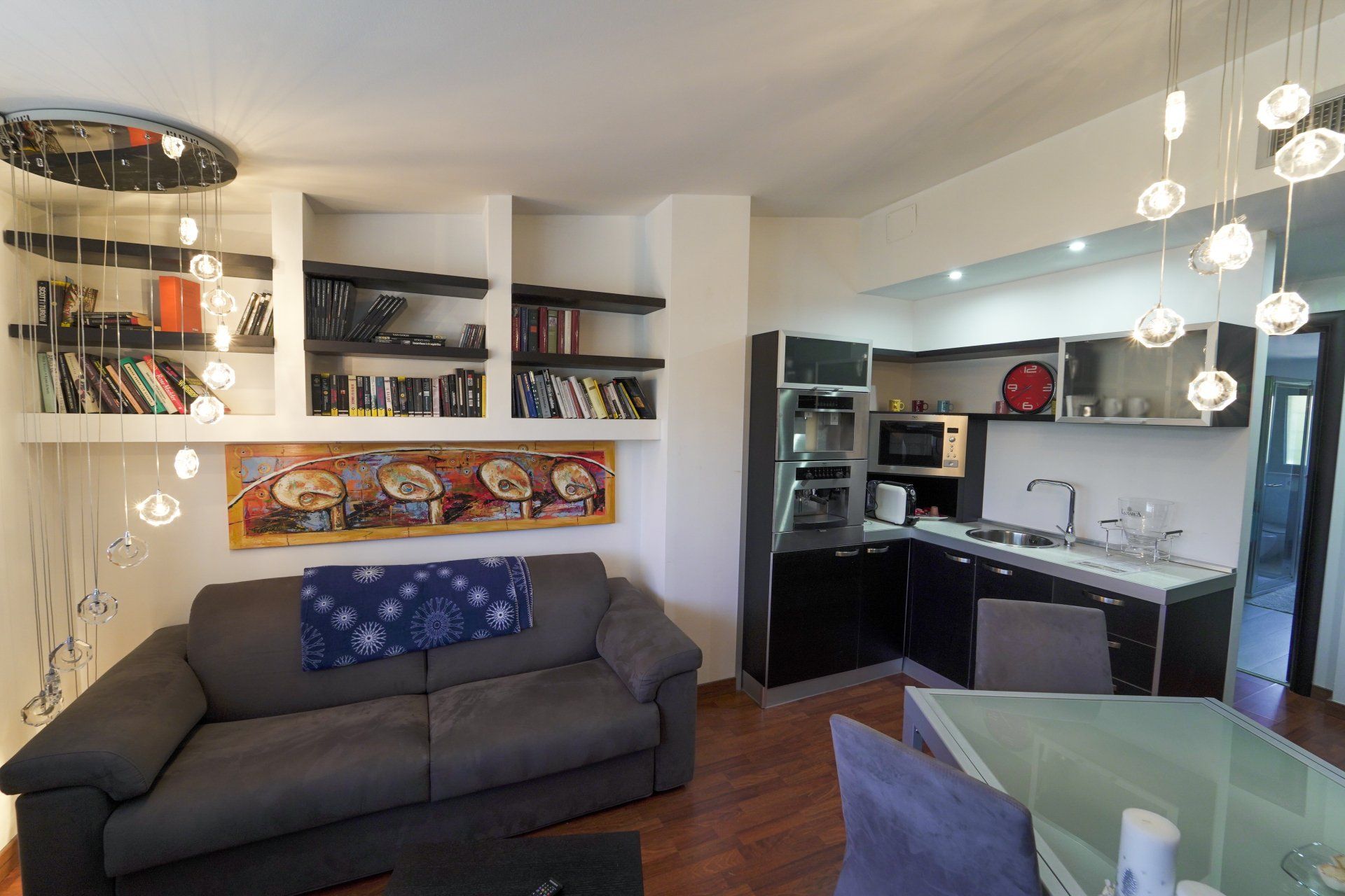 Accogliente soggiorno con librerie integrate, divano grigio scuro e cucina compatta.