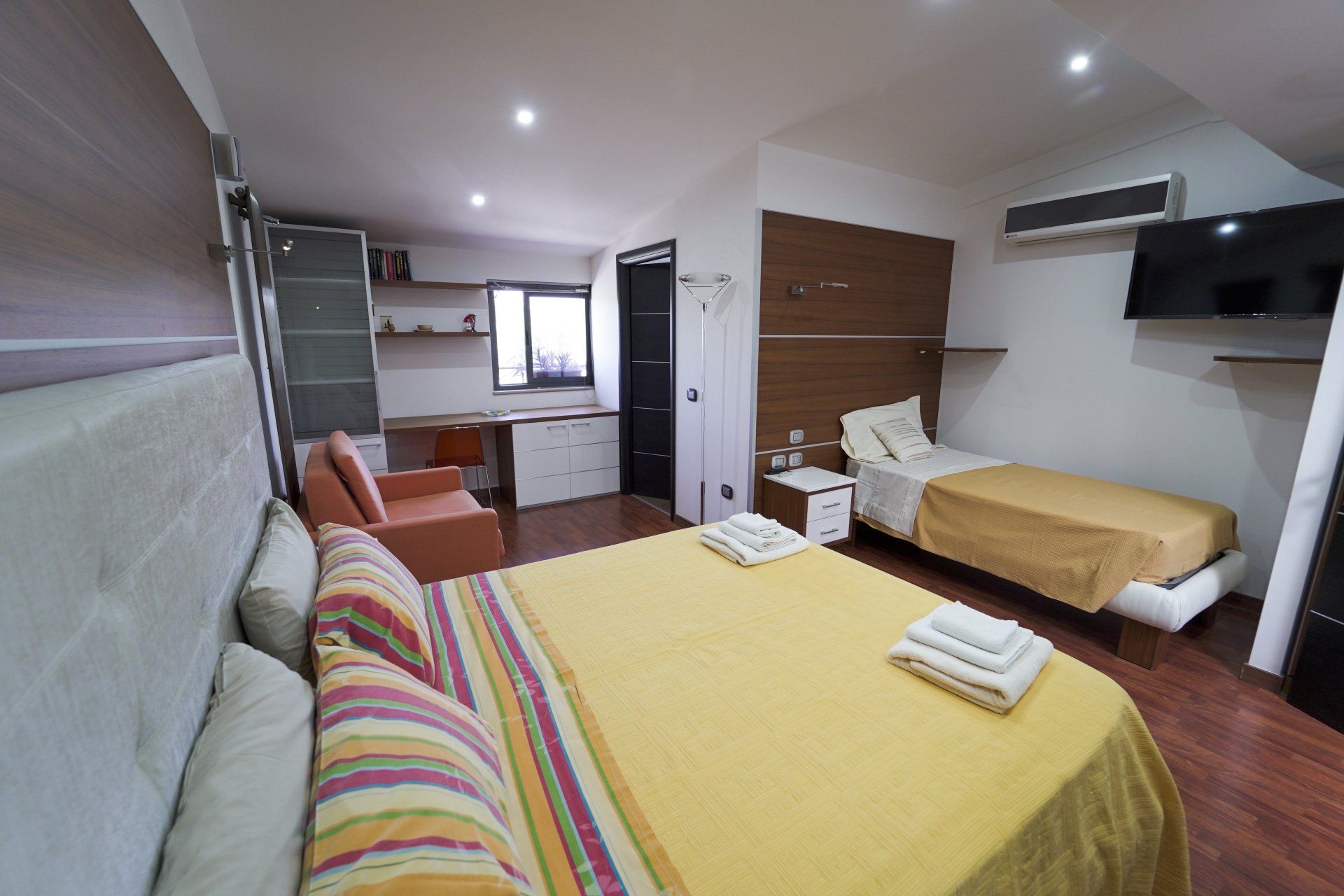 Una luminosa camera d'albergo con letto matrimoniale, letto singolo, scrivania e TV.