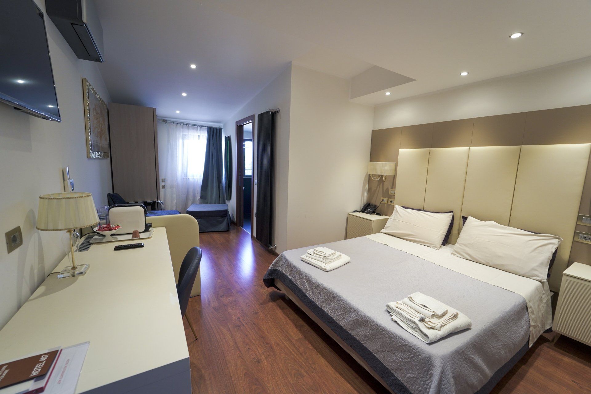 Camera d'albergo con letto, scrivania e zona soggiorno. Illuminazione calda e pavimenti in legno.
