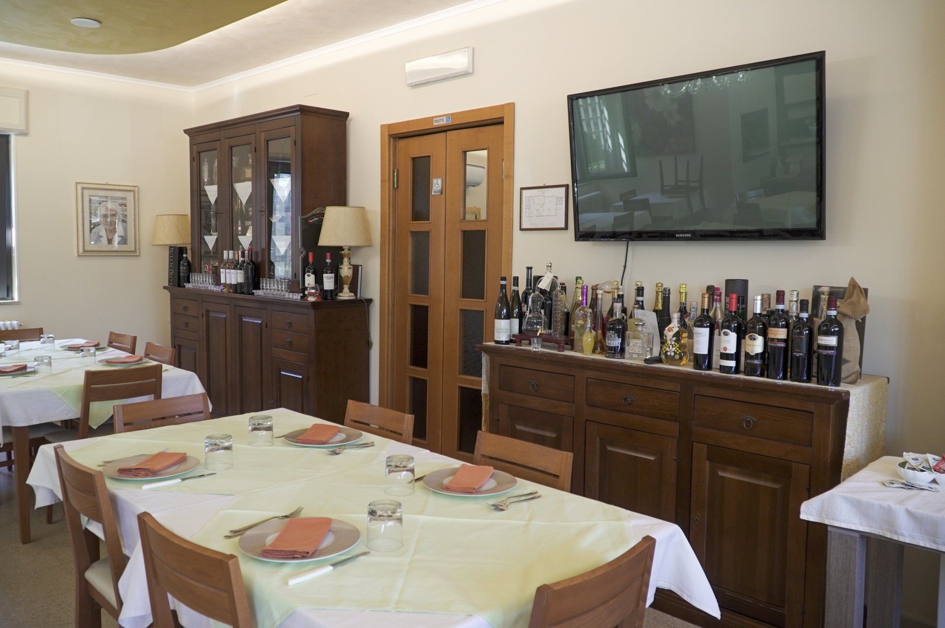 Sala da pranzo del ristorante con tavoli apparecchiati per gli ospiti, mobili in legno e un televisore.