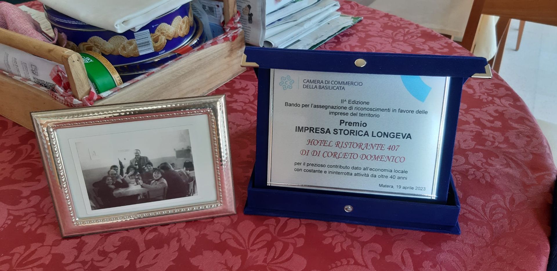 Una foto incorniciata e un premio su una tovaglia rossa. Il premio è in una custodia blu.